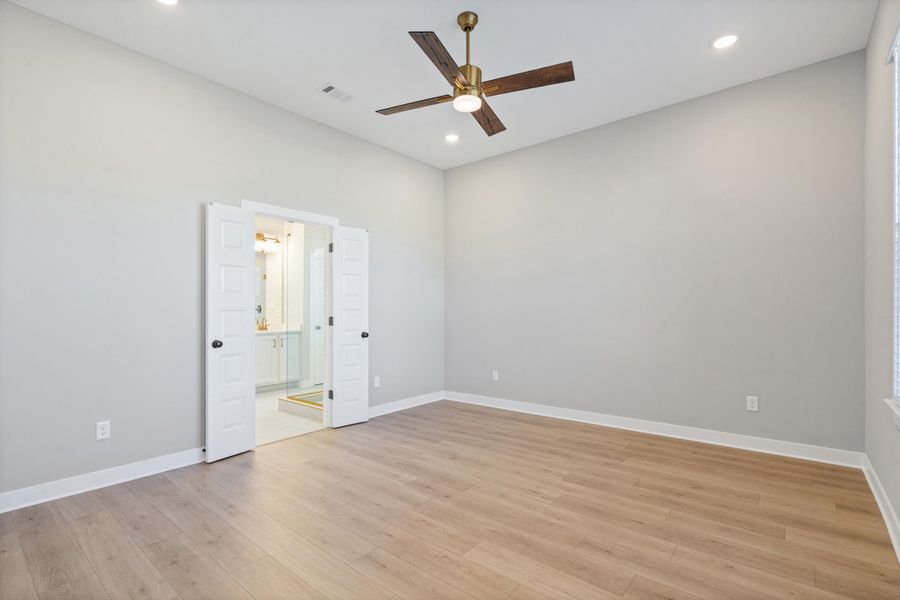Spacious room featuring vaulted ceilings, recessed lighting, wood-finish flooring, a ceiling fan with integrated light, and double doors opening to a bathroom with a glass-enclosed shower