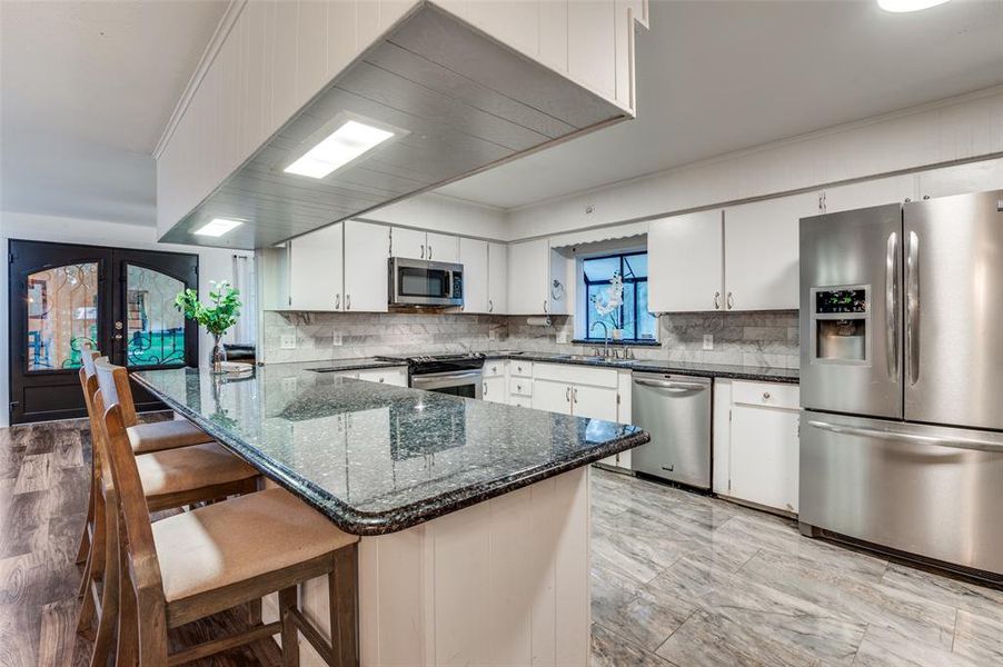 Kitchen with appliances with stainless steel finishes, a sink, backsplash, and white cabinets