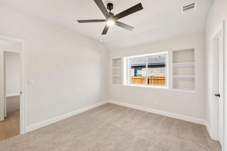 Empty bedroom with carpet, ceiling fan, and built-in wall shelves beside a window