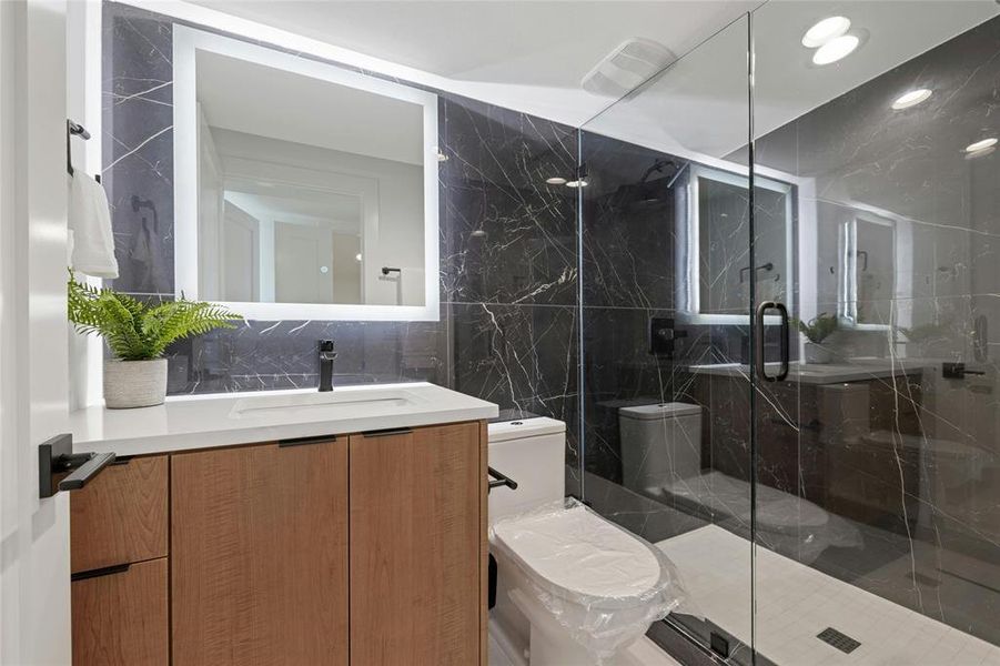 Bathroom with tile walls, toilet, vanity, and a marble finish shower