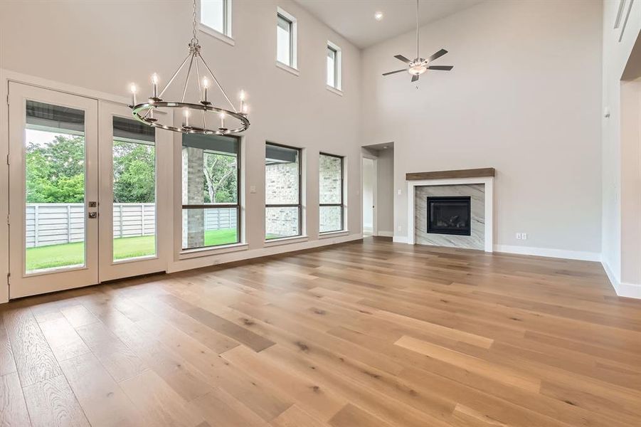 Unfurnished living room with light wood finished floors, a chandelier, a ceiling fan, a premium fireplace, and a towering ceiling Unfurnished living room with light wood finished floors, a chandelier, a ceiling fan, a premium fireplace, and a towering ceiling