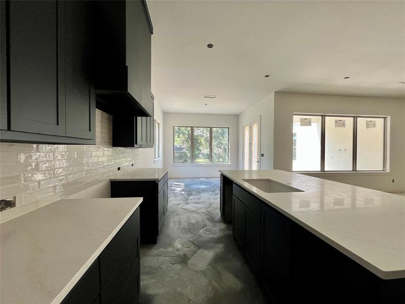 Kitchen with backsplash, sink, concrete flooring, and light stone countertops