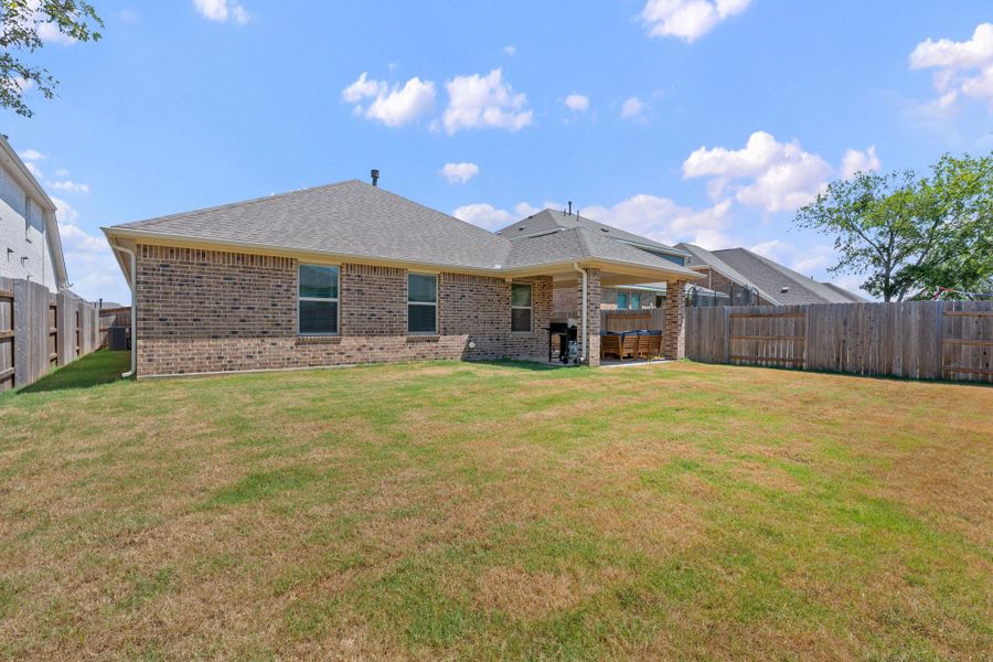Rear view of house with a fenced backyard, a shingled roof, brick siding, and a patio Rear view of house with a fenced backyard, a shingled roof, brick siding, and a patio