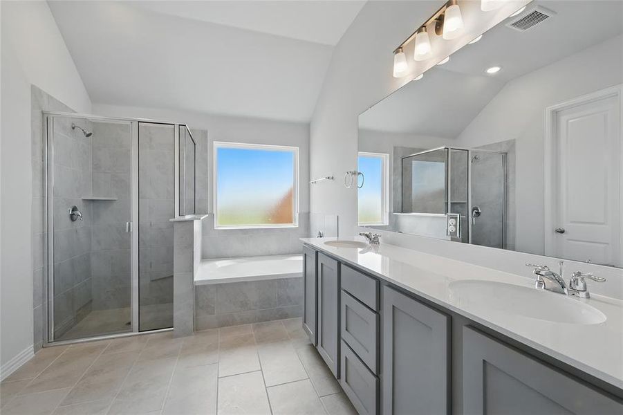 Full bathroom featuring lofted ceiling, double vanity, a shower stall, a bath, and light tile patterned floors