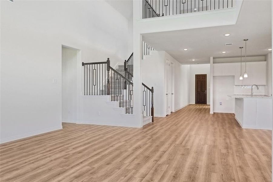 Unfurnished living room with light wood-type flooring, a towering ceiling, and sink