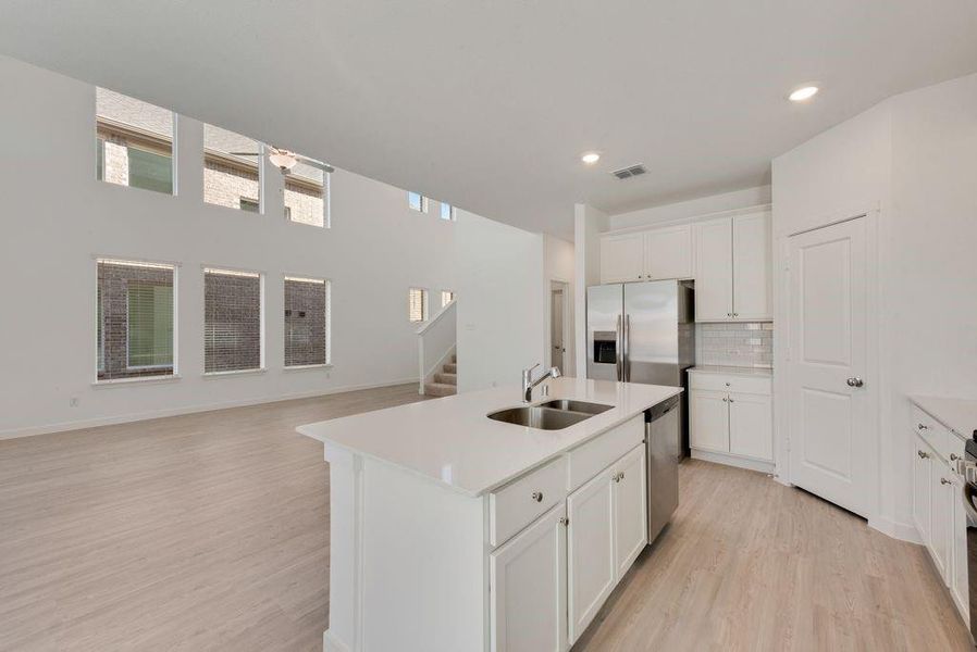 Kitchen featuring light wood-style flooring, appliances with stainless steel finishes, light countertops, decorative backsplash, and white cabinets Kitchen featuring light wood-style flooring, appliances with stainless steel finishes, light countertops, decorative backsplash, and white cabinets