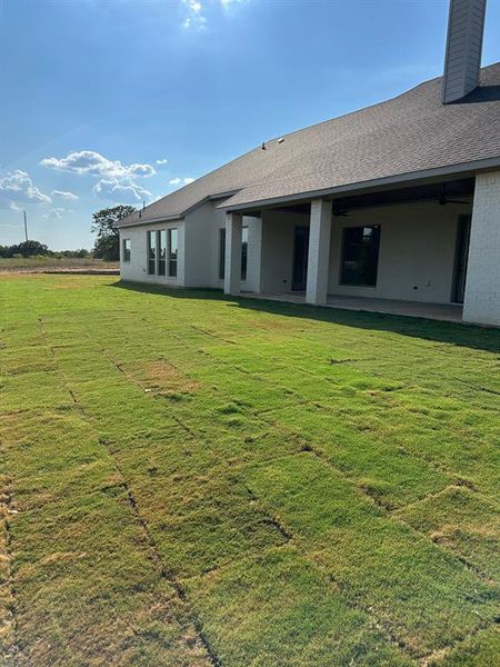 Rear view of property with a patio area, brick siding, a yard, a chimney, and roof with shingles