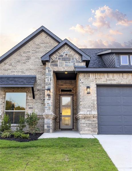 French country inspired facade featuring brick siding, a garage, a front yard, and driveway