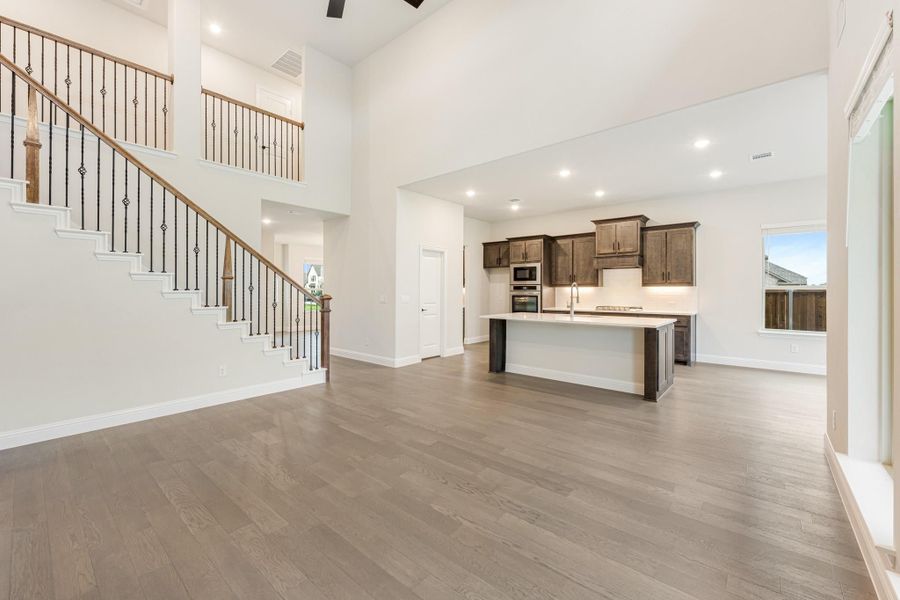 Open living area with hardwood floors, two-story staircase, and kitchen with dark wood cabinets and center island Open living area with hardwood floors, two-story staircase, and kitchen with dark wood cabinets and center island