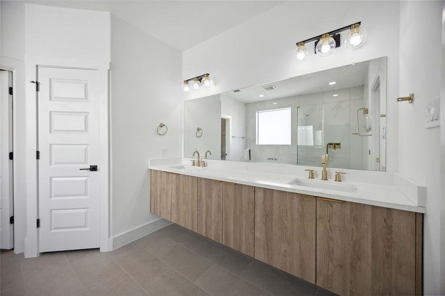 The primary bathroom offers a double vanity, large mirror, ample lighting, and a glass-enclosed shower. The design features clean lines, light cabinetry, and a neutral color palette.