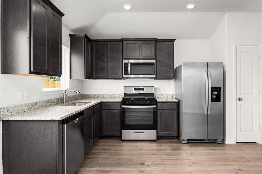 Kitchen featuring appliances with stainless steel finishes, a sink, light wood-style floors, and light stone countertops Kitchen featuring appliances with stainless steel finishes, a sink, light wood-style floors, and light stone countertops