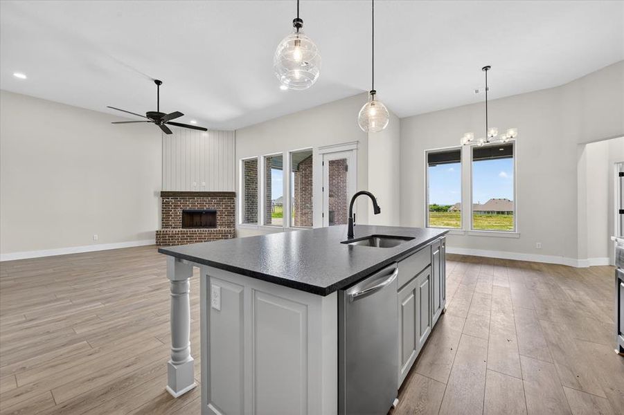 Kitchen with a center island with sink, dishwasher, open floor plan, light wood-style floors, and a fireplace