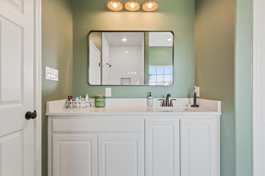 Bathroom with a textured wall, vanity, and tiled shower