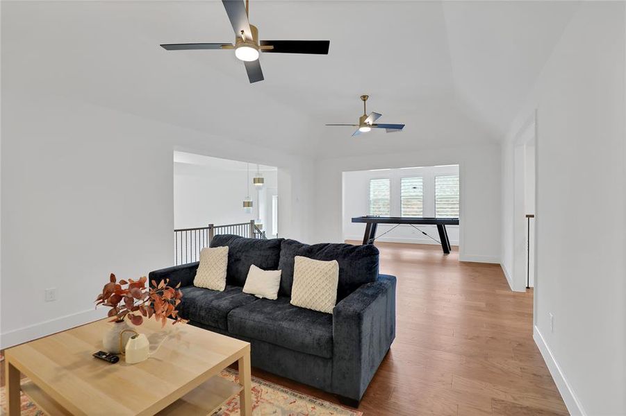 Open-concept room featuring wood-finish flooring, vaulted ceilings, and contemporary ceiling fans