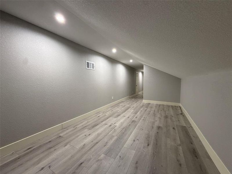 Bonus room with a textured ceiling, a textured wall, recessed lighting, and light wood-style flooring