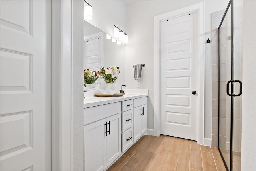 Full bath with light wood-style floors, double vanity, and a stall shower