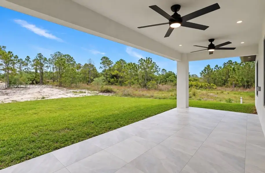 Covered patio featuring large-format porcelain tile flooring, dual ceiling fans with integrated lighting, recessed lighting, and a rear yard bordering natural vegetation Covered patio featuring large-format porcelain tile flooring, dual ceiling fans with integrated lighting, recessed lighting, and a rear yard bordering natural vegetation