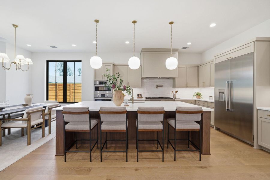 Kitchen with an island with sink, a kitchen bar, stainless steel appliances, light wood-style floors, and light stone countertops