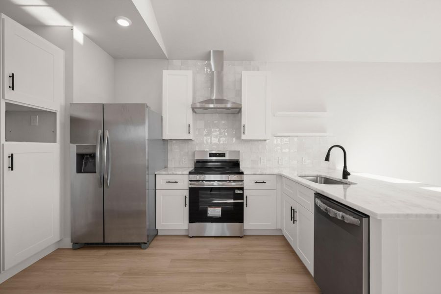Kitchen with stainless steel appliances, a peninsula, white cabinets, light stone counters, and light wood-style floors