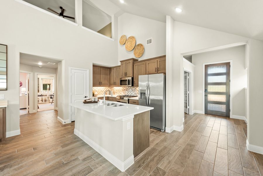 Open kitchen with center island, brown cabinets, stainless appliances, and high ceilings above wood-look tile floors