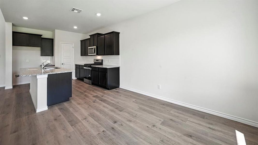 Modern kitchen featuring dark cabinetry, stainless steel appliances, a center island with sink, granite countertops, and wood-finish flooring Modern kitchen featuring dark cabinetry, stainless steel appliances, a center island with sink, granite countertops, and wood-finish flooring