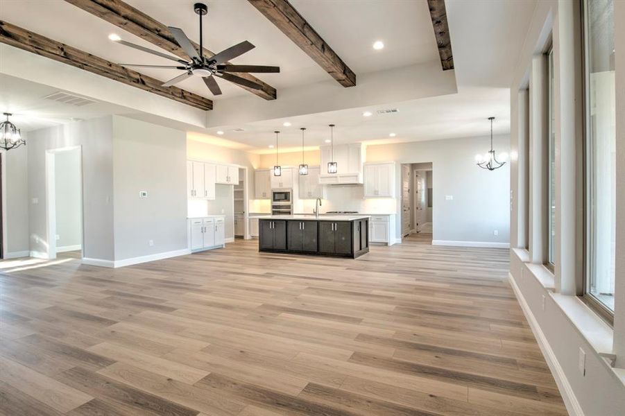 Unfurnished living room featuring beamed ceiling, ceiling fan with notable chandelier, light hardwood / wood-style flooring, and sink