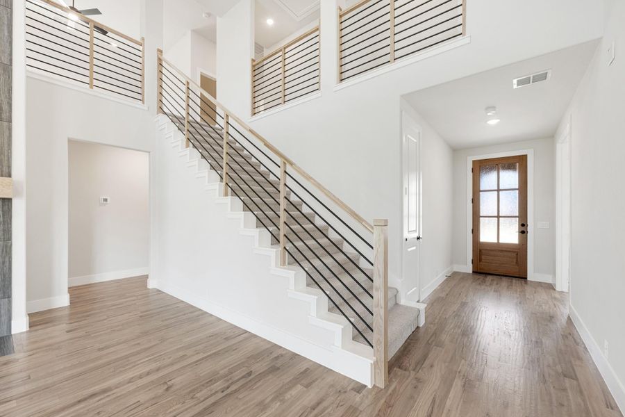Two-story entryway with open staircase, metal rod railings, wood floors, and wood front door with glass panels