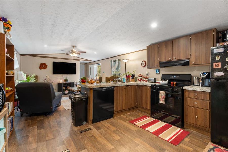 Kitchen with black appliances, under cabinet range hood, wood finished floors, a peninsula, and light countertops Kitchen with black appliances, under cabinet range hood, wood finished floors, a peninsula, and light countertops