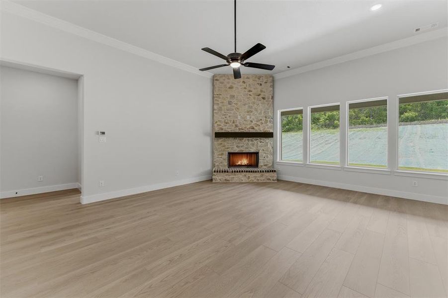 Spacious room featuring a stone fireplace with a wood mantle, wood-finish flooring, a ceiling fan, and a wall of four windows