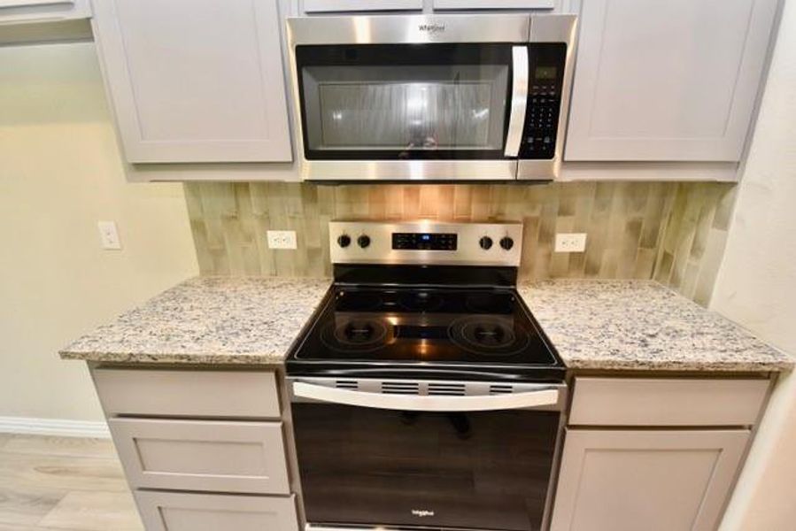 Kitchen featuring stainless steel appliances, tasteful backsplash, light stone counters, and light wood-style flooring