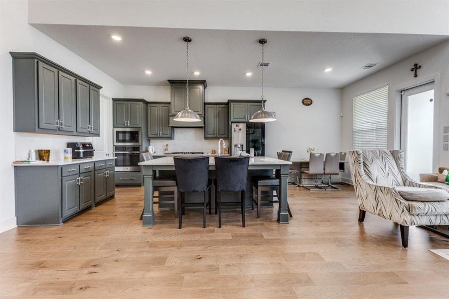 Kitchen featuring an island with sink, decorative light fixtures, stainless steel appliances, gray cabinets, and tasteful backsplash