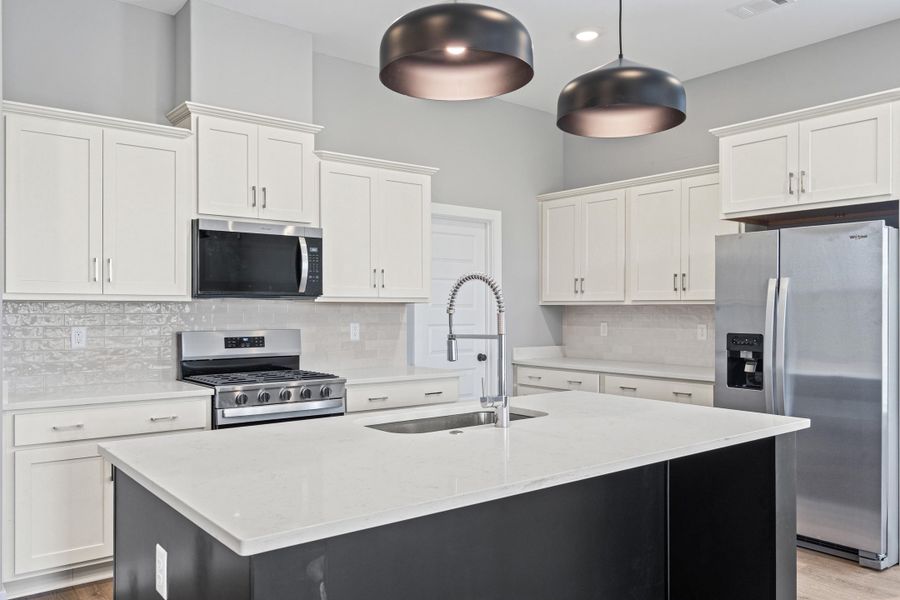 Kitchen featuring stainless steel appliances, a kitchen island with sink, light stone counters, tasteful backsplash, and two tone cabinetry