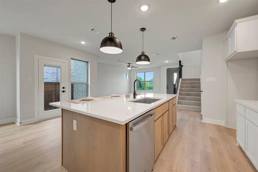 Kitchen island featuring a stainless steel sink with a matte black faucet, integrated dishwasher, and pendant lighting