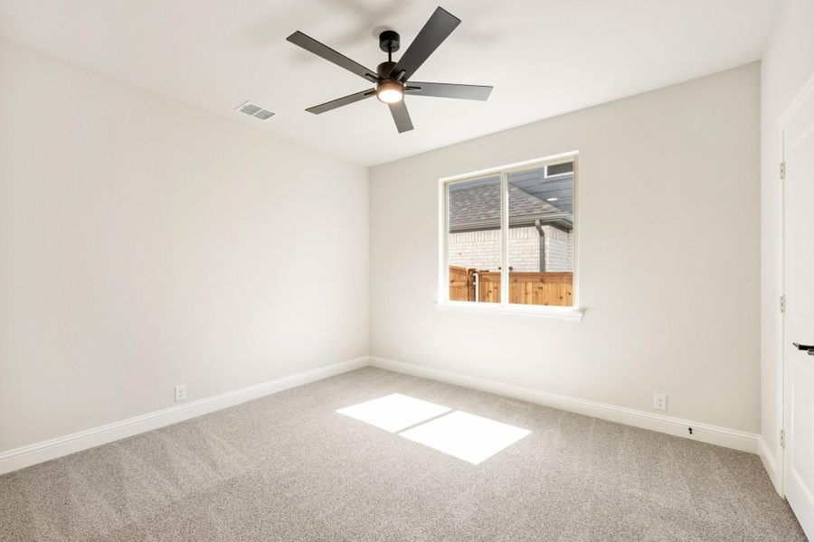 Empty bedroom with gray carpet, ceiling fan, and single window with backyard view
