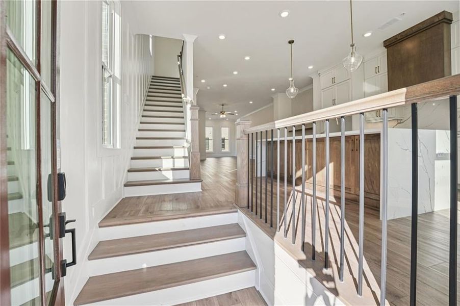 Front brownstone entry point for the Chamberlain plan opens to wood finished stairs, hardwood floors, recessed lighting, a ceiling fan, crown molding. Image is of previously built Chamberlain plan.