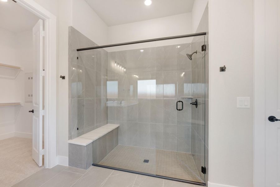 Large walk-in shower with gray tile walls, glass door, and built-in bench seat