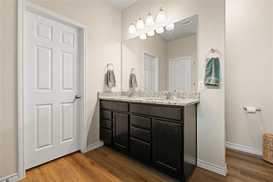 Full bathroom featuring dark wood-type flooring, double vanity, and a textured wall