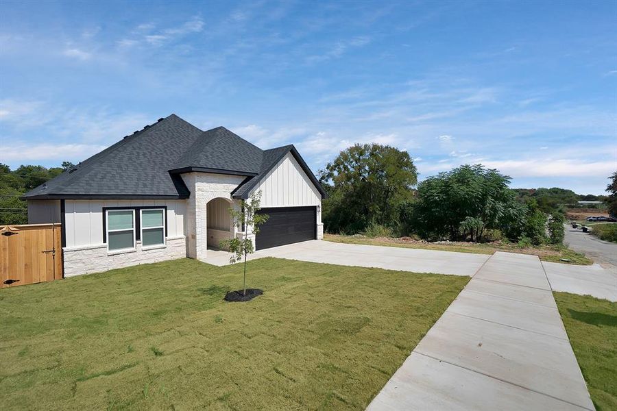View of front of house with stone siding, a shingled roof, concrete driveway, and a front yard View of front of house with stone siding, a shingled roof, concrete driveway, and a front yard