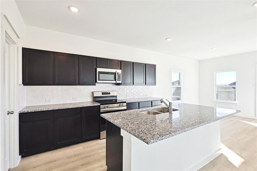 Kitchen with light stone counters, light hardwood / wood-style floors, a kitchen island with sink, sink, and stainless steel appliances