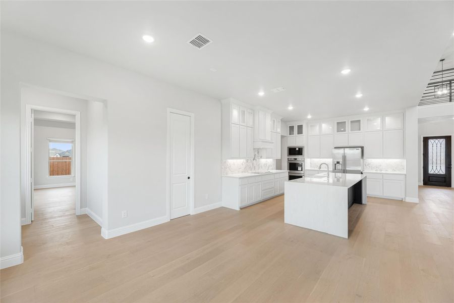 Open kitchen with white cabinets, center island, stainless steel appliances, and light hardwood floors