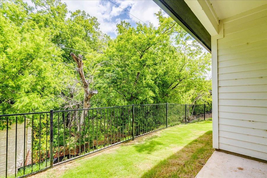 A verdant vista extends beyond the private yard, bordered by a sleek iron fence.