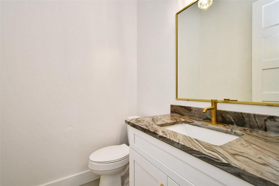 A chic guest bathroom featuring a bold stone countertop with rich veining and high-end gold hardware.