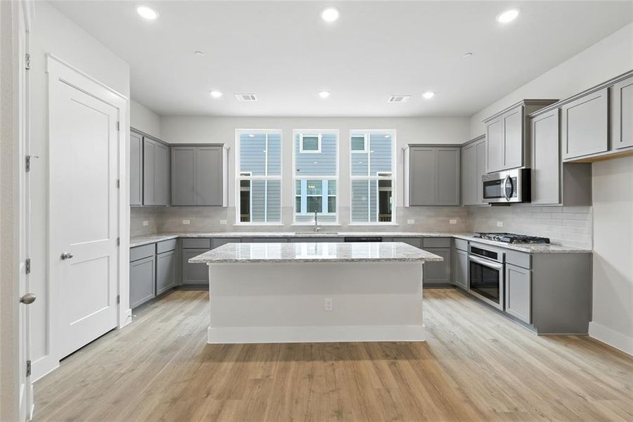 Kitchen featuring gray cabinetry, a kitchen island, tasteful backsplash, recessed lighting, and light wood-style flooring