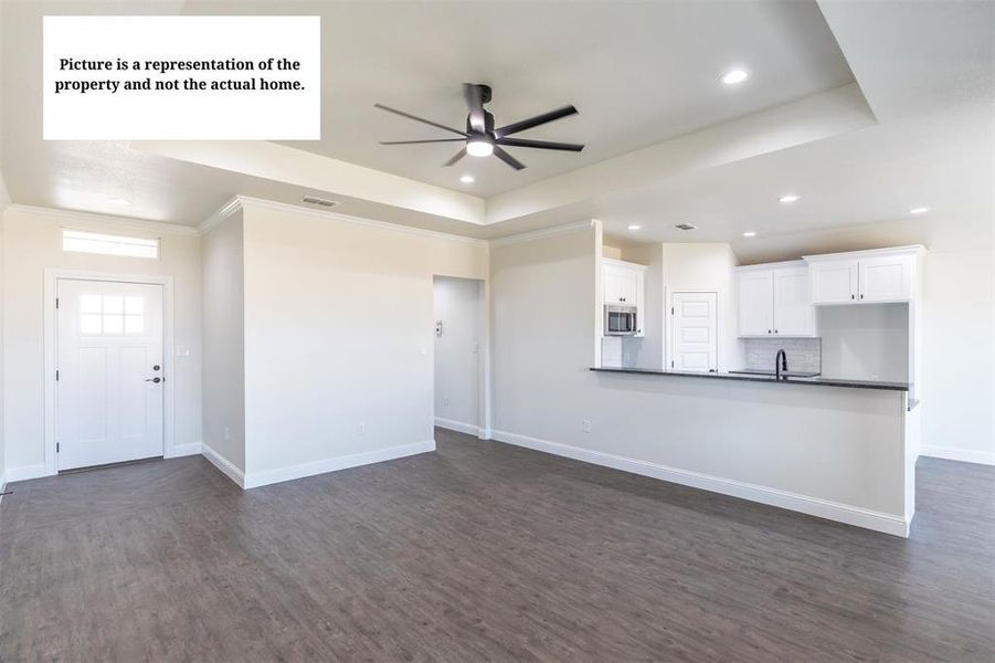 Open-concept living area with wood-finish flooring, tray ceiling, and modern ceiling fan