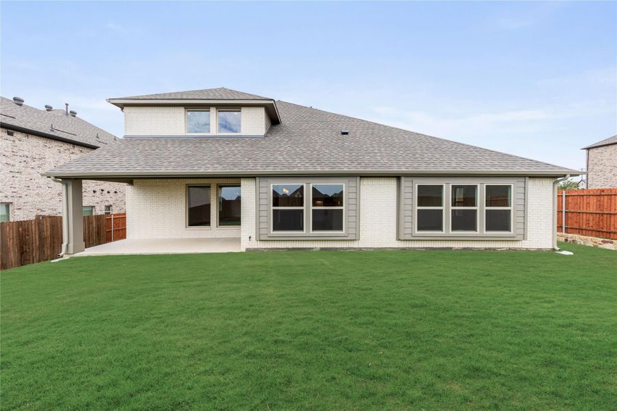 Rear exterior of brick home with large windows, covered patio, and fenced backyard with green lawn