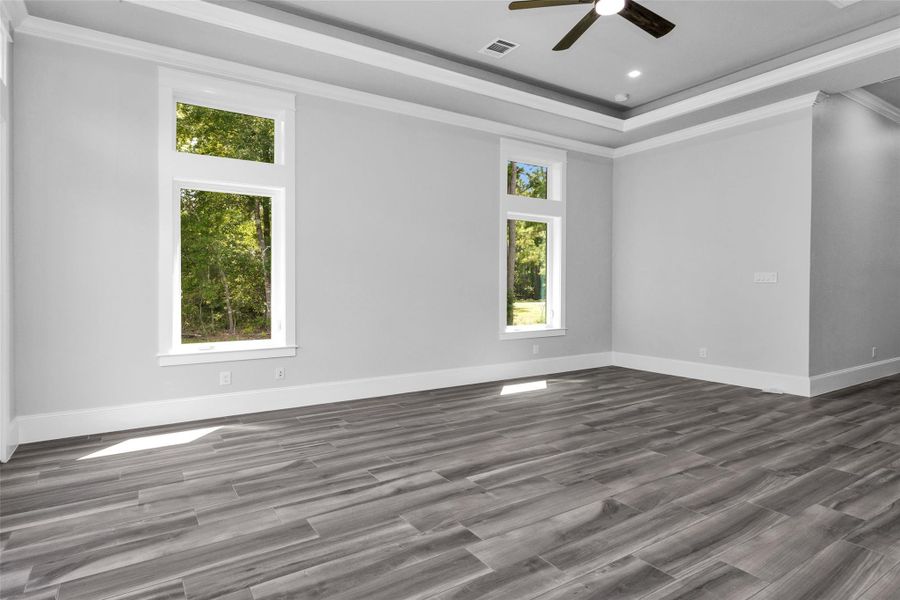 The Primary Suite glows under abundant natural light from multiple windows, and an elegant coffered ceiling that adding architectural interest.