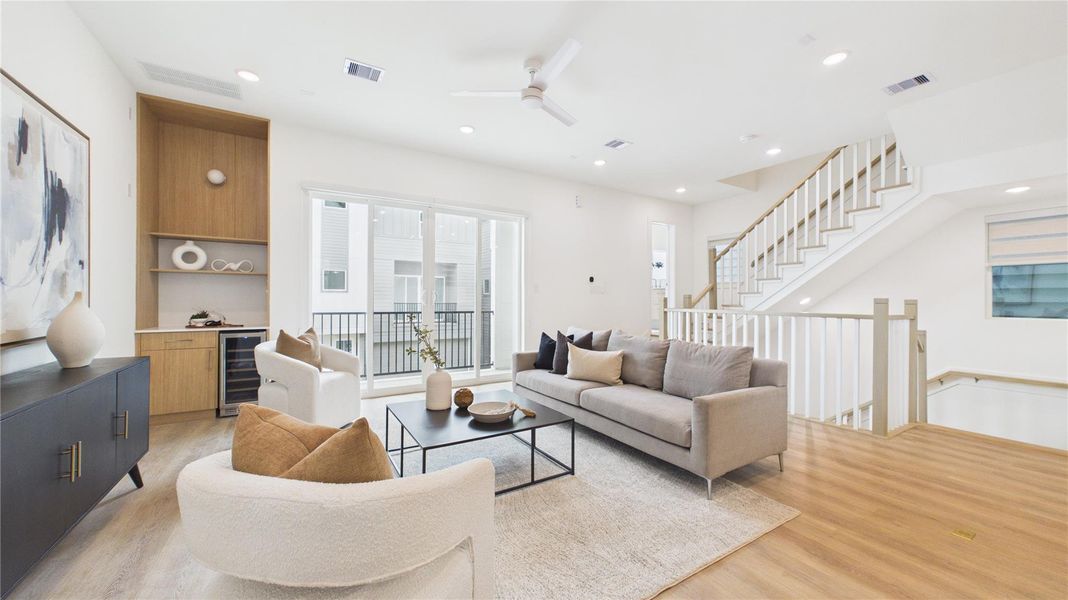 Bright and airy living room with modern decor, featuring a neutral color palette, hardwood floors, and large windows. Includes a cozy seating area, built-in shelving, and an open staircase.