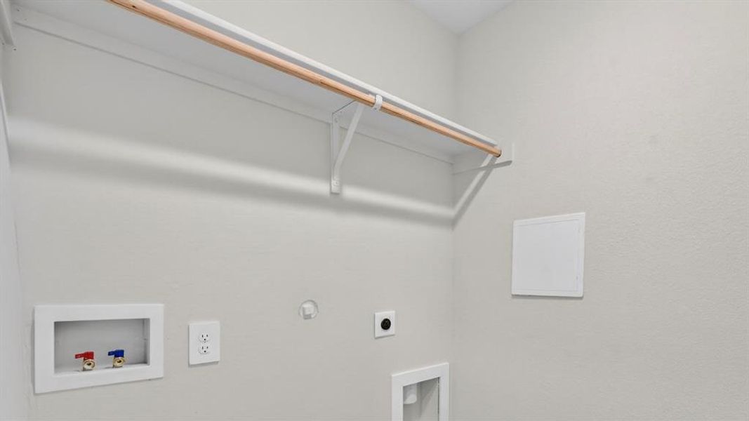 Dedicated laundry area featuring a built-in hanging rod, wall-mounted shelving, and utility hookups for appliances
