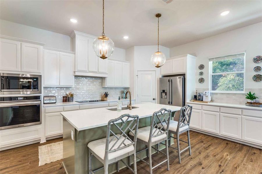 Kitchen featuring white cabinets, appliances with stainless steel finishes, pendant lighting, and an island with sink