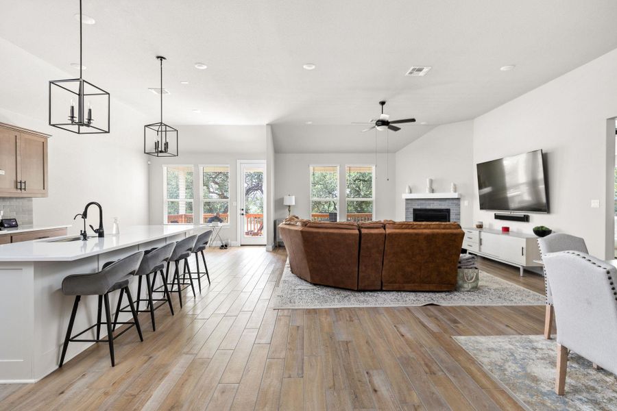 Living area with light wood-style flooring, lofted ceiling, a brick fireplace, ceiling fan, and a chandelier